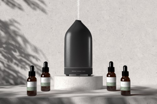 En elegant svart diffuser omgitt av fire små brune flasker med dråpetenter på en betongbakgrunn.