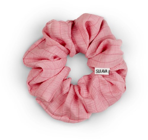 A pink fabric scrunchie with a small white tag labeled "SUI AVA".