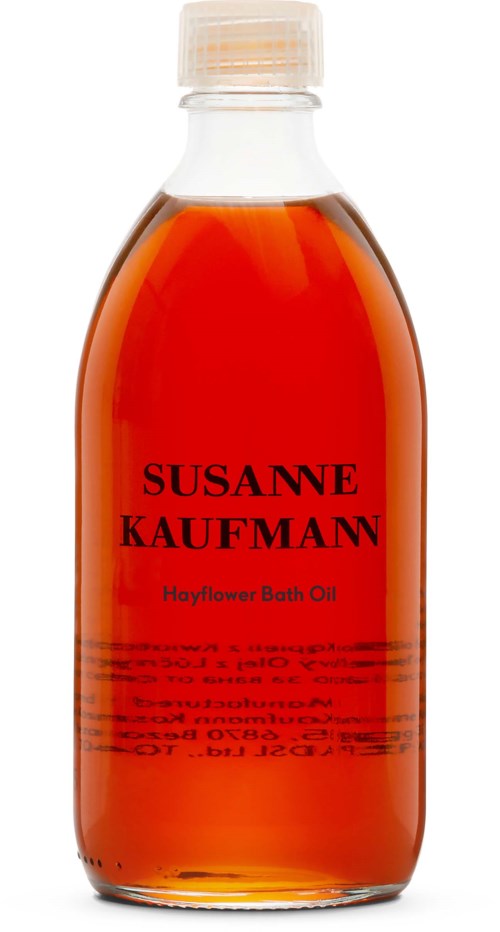 En klar flaske med oransje badolje, merket med navnet Susanne Kaufmann og produktnavnet Hayflower Bath Oil.