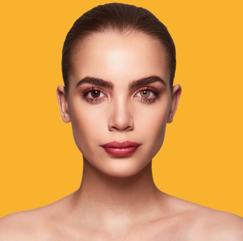 Porträt einer Frau mit Make-up vor gelbem Hintergrund.