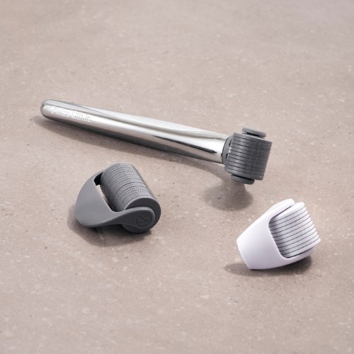En massagerulle, en handhållen enhet och en vit och grå massager ligger på en simpel yta.