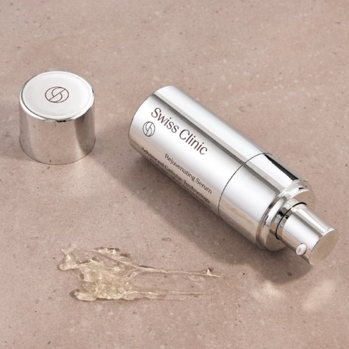 En silverflaska märkt 'Swiss Clinic' med serum utanför på en beige yta.