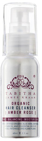 Een witte fles met pomp, gelabeld 'Tabitha Organic Hair Cleanser Amber Rose', in eendoorzichtige plastic verpakking.
