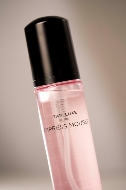 En tydlig rosa flaska med svart lock, märkt 'TAN-LUXE EXPRESS MOUSSE'.