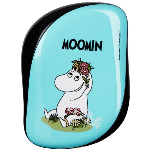 Muumihahmo istuu kukkien keskellä, pitää kukkaa päänsä päällä, taustalla sininen väri ja 'MOOMIN'-teksti.