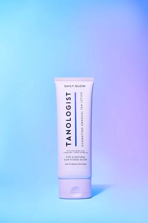Eine weiße Tube Tanologist Daily Glow Lotion steht vor einem gradienten blauen bis lila Hintergrund.