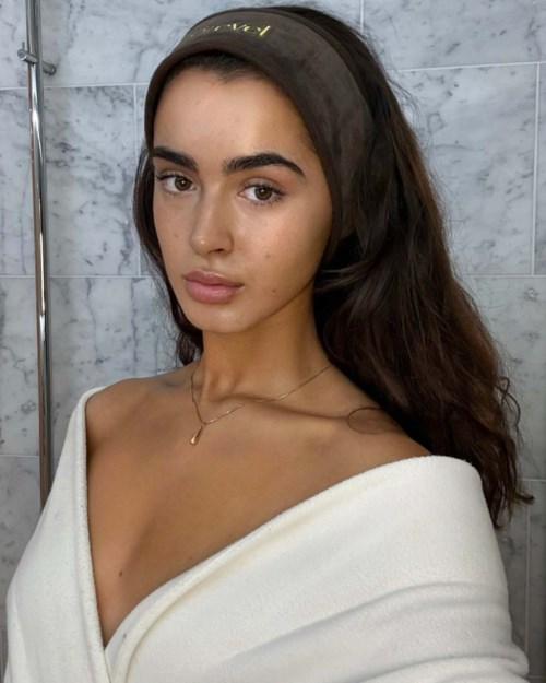 A young woman with long dark hair, wearing a black headband and a white off-shoulder top.