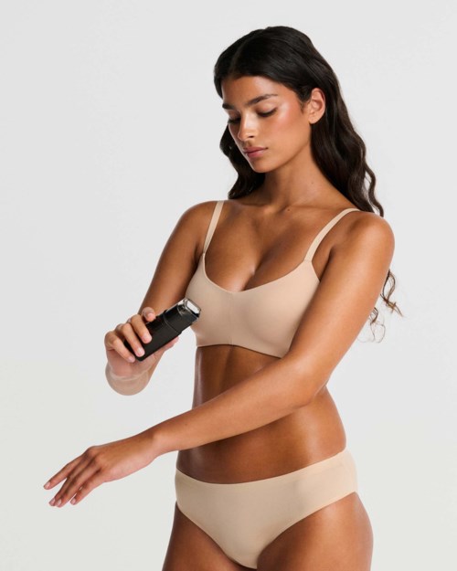 Woman in beige underwear using an electric razor on her arm.