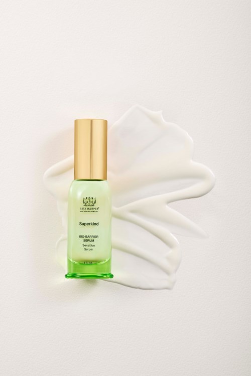 A small green skincare bottle with a gold cap, placed on cream spilled on a white background.