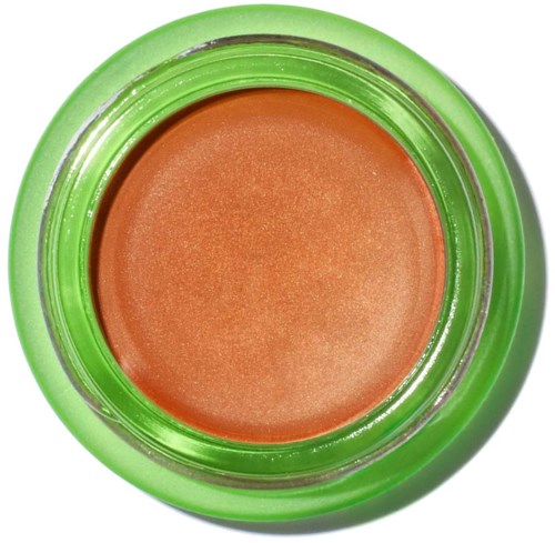 En grön behållare med en persikofärgad kräm eller makeupprodukt inuti. Behållaren har ett genomskinligt lock.