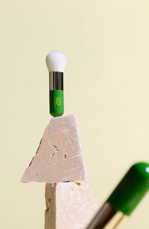 A green and silver pen balanced on top of two beige rocks, with a white sphere on the pen's tip.