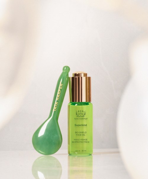 A green bottle with a gold cap and a green spoon-shaped tool beside it. The bottle is labeled with skincare product details.