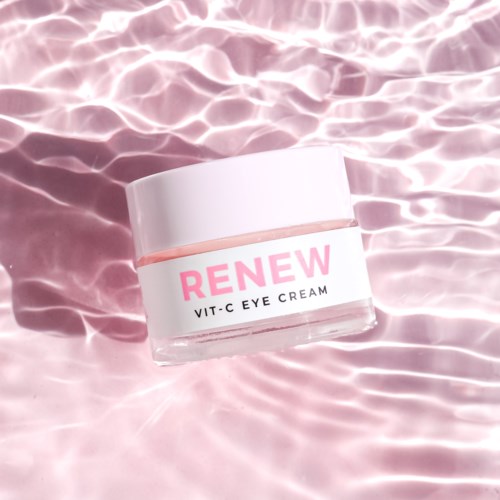 En liten burk märkt 'RENEW VIT-C EYE CREAM' svävar på rosa vatten med ljusreflexer.