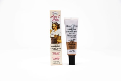 En tube med flydende concealer og dens kasse, begge mærket med mærket Anne T. Dotes, på hvid baggrund.