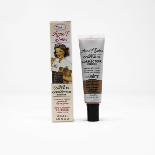 Et tube og en æske med theBalm Anne T Dotes flydende concealer med vintage kvindeillustration. Æsken viser produktdetaljer og mærke.