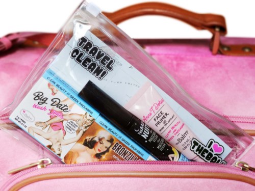 Eine durchsichtige Tasche enthält Reisegrößen von Hautpflege- und Make-up-Produkten in einer pinken Tasche.