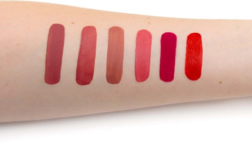 Six red lipstick swatches on arm, varying from light to dark shades of red.