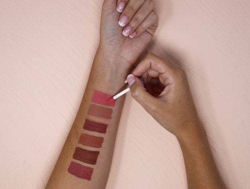 Someone is testing skin tone makeup shades on their arm with a swab. There are seven color samples in a row.