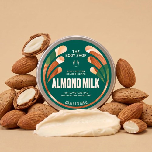 En rund beholder med mandelmelk kroppssmør omgitt av mandler og en stripe av kremen.