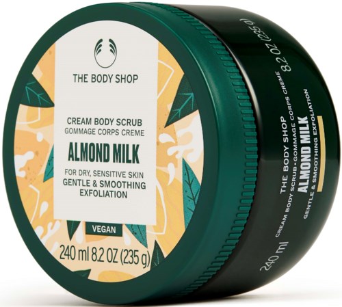 En grön rund behållare från The Body Shop med mandelmjölkskrubb för torr hy, 240 ml, vegansk, med blad och orange design.