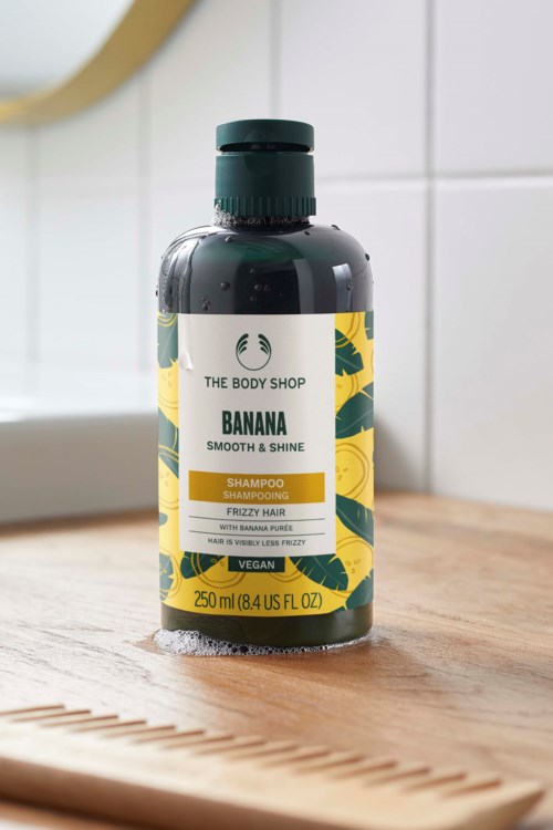 Bananasampoo pullasampoota sileisiin, kiiltäviin ja pörröisiin hiuksiin, vihreällä ja keltaisella etiketillä ja mustalla korkilla.