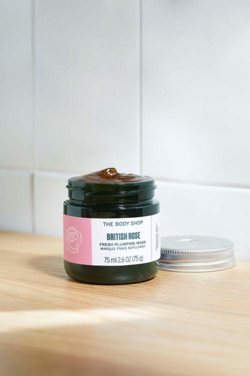 Et glass fra The Body Shop British Rose ansiktsmaske på en treoverflate, med lokket ved siden av.