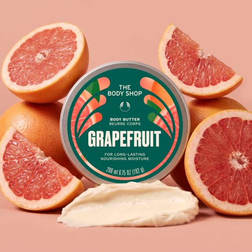 Bodylotionkrukke med grapefruktduft omgivet av ferske grapefruktbåter på en ferskenfarget bakgrunn.