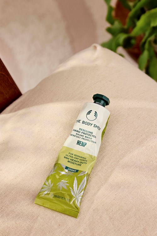 A tube of hemp hand rescue cream on beige fabric with green plants in the background.