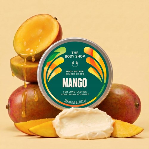Ein boks med mango-doftende kroppssmør, omgitt av hele og skivede mangoer med litt smeltende mango juice.