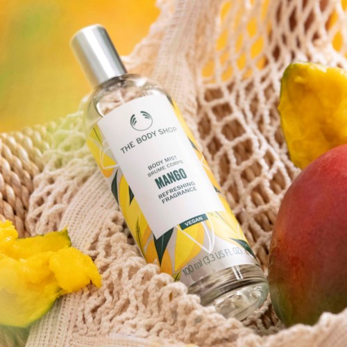en mango doft kroppsspray i en klar flaska på en beige tyg med mango- och anansskivor i närheten.