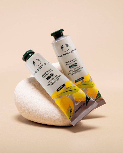 Två tuber handkräm med smak av mango från The Body Shop vilar på en slät vit stenyta.