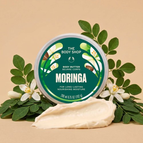 Moringa kroppssmørkrukke med krem som er spredt og grønne blader og hvite blomster rundt den.