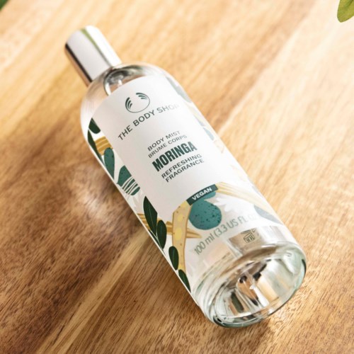En klar sprayflaske med lokk, merket som 'Moringa Refreshing Fragrance', ligger på en treoverflate.