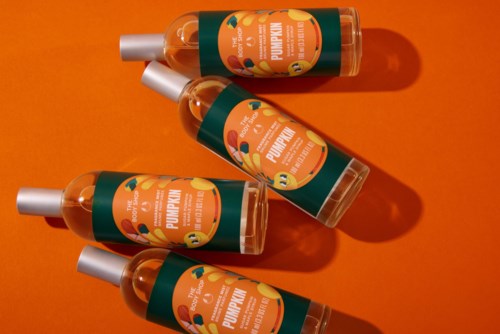 Fyra orange flaskor med pump i pumpkin body oil finns på en orange bakgrund, och kastar skuggor.