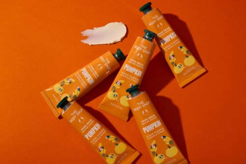 Four orange tubes of pumpkin body lotion with green caps, one smeared white lotion on orange background.