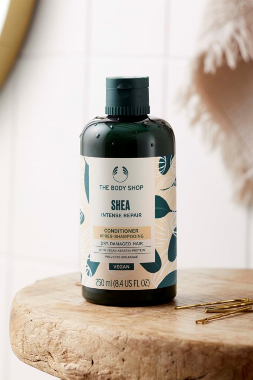 Tummanvihreä Shea Intense Repair -hoitoainepullo puisen pinnan päällä, lähellä.