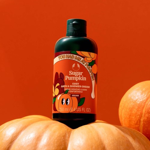 Een zwarte fles met pompoengeurige bad- en douchecrème met oranje en groene label op pompoenen.
