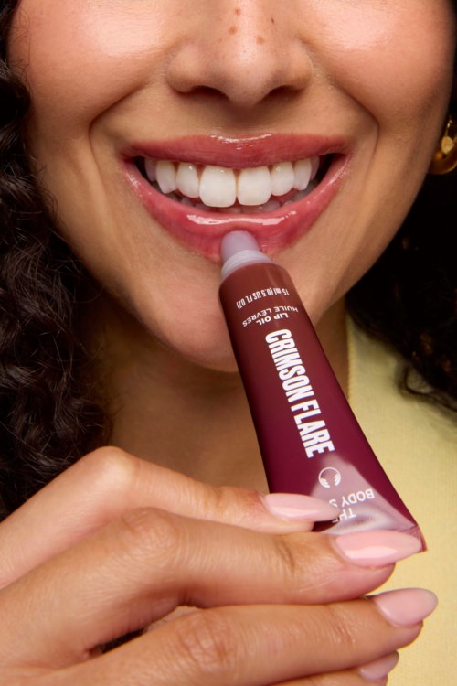 Een lachende vrouw brengt lipgloss aan met een stick die GLOSSY FLARE heet.