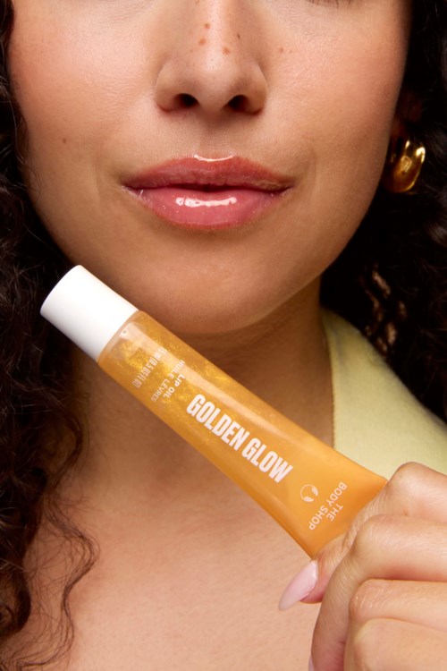 Een vrouw houdt een gele tube met Golden Glow dichtbij haar gezicht.