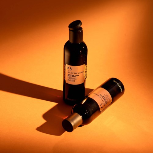 Two dark bottles with labels are placed on an orange background, creating shadows. One bottle is upright, the other is lying down.
