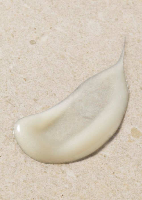 En droppe vit lotion eller kräm på en beige yta.