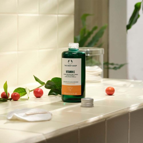 En flaske med Vitamin C-toner på en flislagt overflate med spredte røde bær og en grå hettel.