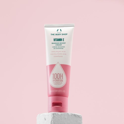 Obraz przedstawia różowo-biały tubkę kremu Vitamin E od The Body Shop na białym stojaku na różowym tle.