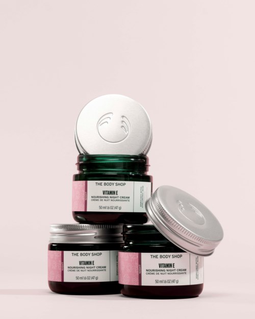 Tre burkar med The Body Shop Vitamin E nattkräm staplade, en burk är öppen och visar produkten inuti.