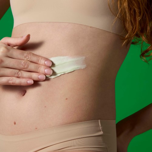 Person applying lotion or cream to their abdomen against a green background.