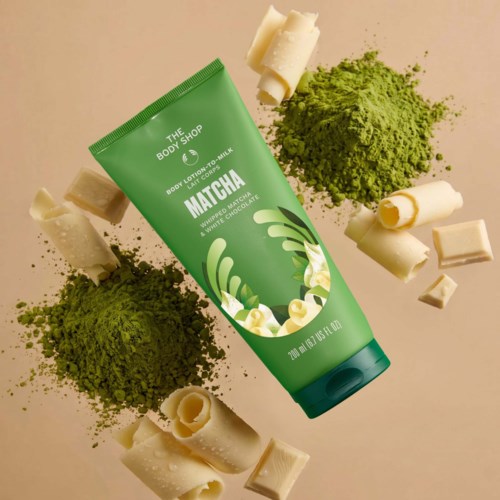 En grön tube av kroppslotion från The Body Shop omgiven av matcha pulver, vita chokladbitar och matcha-färgade föremål.
