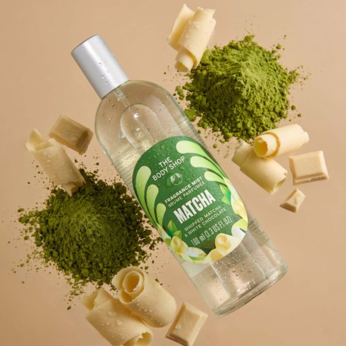 A clear bottle labeled Matcha, surrounded by green matcha powder and white chocolate pieces.