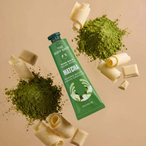 Matcha-Duft-Hand- und Nagelbalsam-Tube umgeben von weißen und grünen Schokoladenstücken und Matchapulver.
