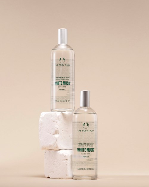 Kaksi White Musk -tuoksuspraypullot ovat valkoisten kivien päällä vaalean beigen taustan edessä.
