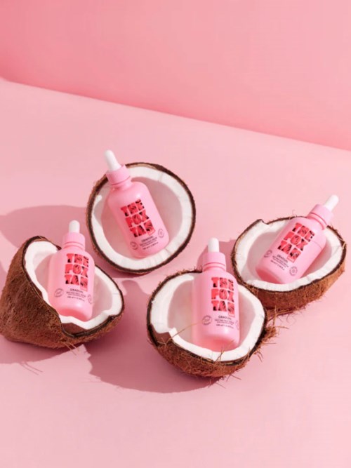 Four pink bottles are placed inside coconut shells on a pink background.